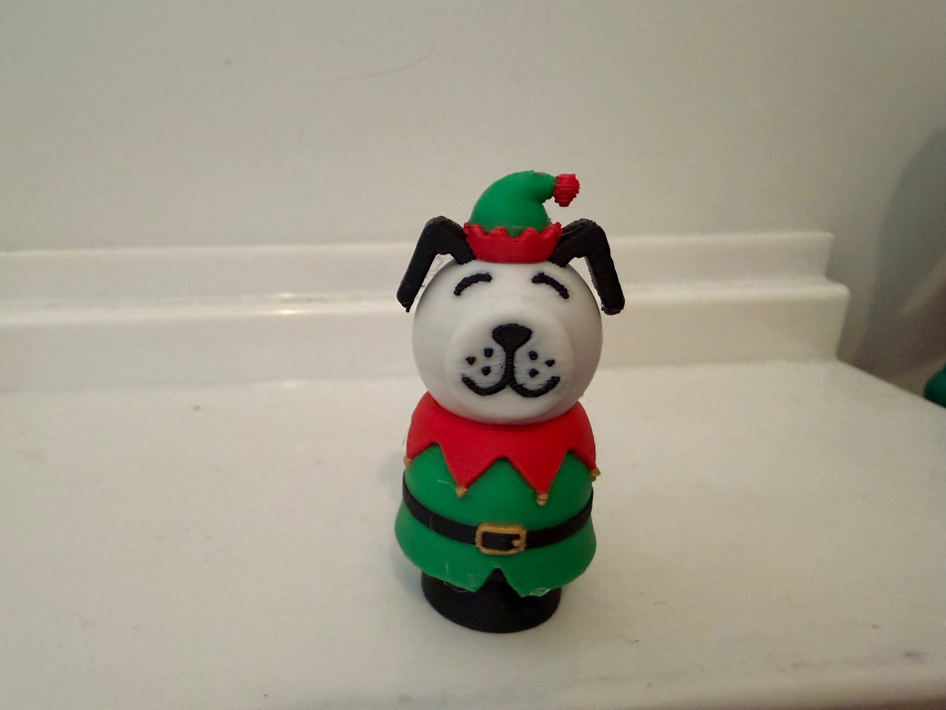 Front view of holiday dog figurine with green hat, red top, and gold belt