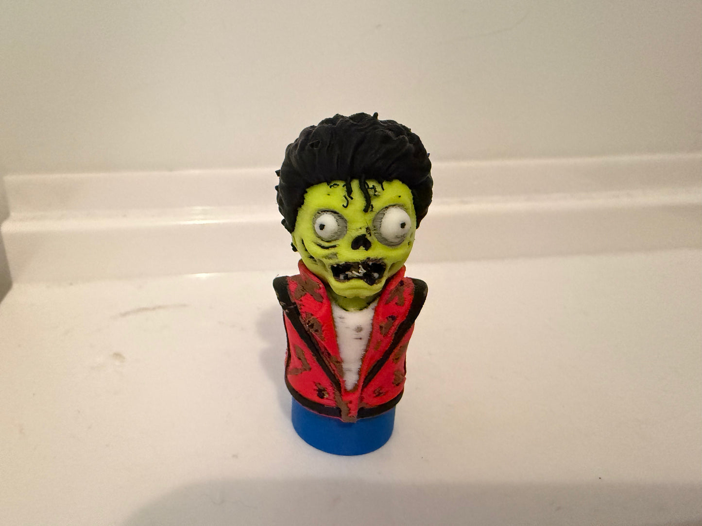 Zombie bust collectible figurine with black hair, green face, red jacket, blue base