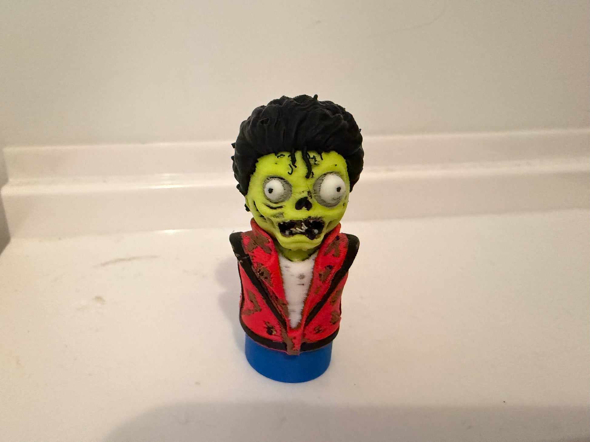 Zombie bust collectible figurine with black hair, green face, red jacket, blue base