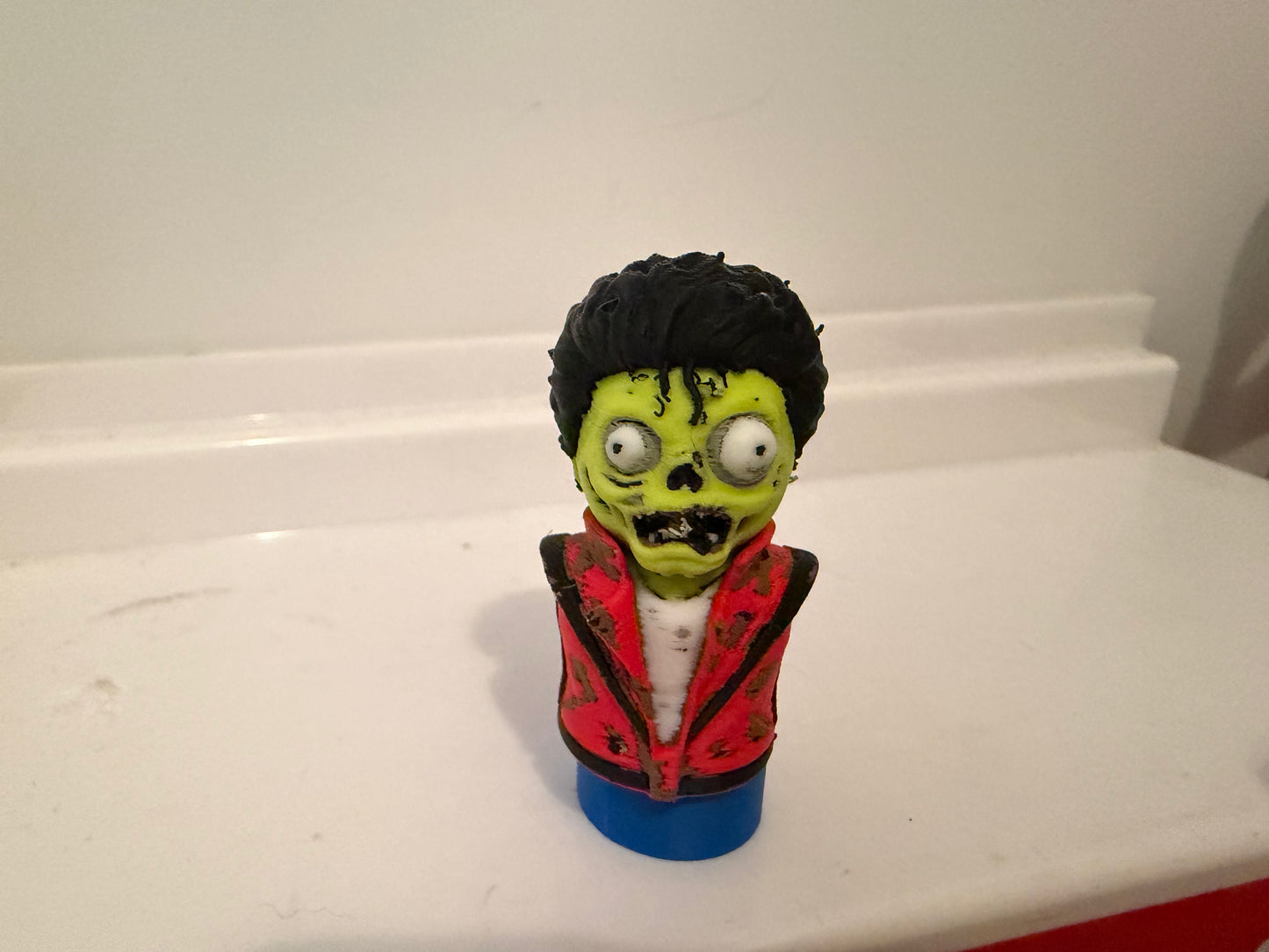 Zombie bust collectible with green face, black hair, red jacket over white shirt, blue base