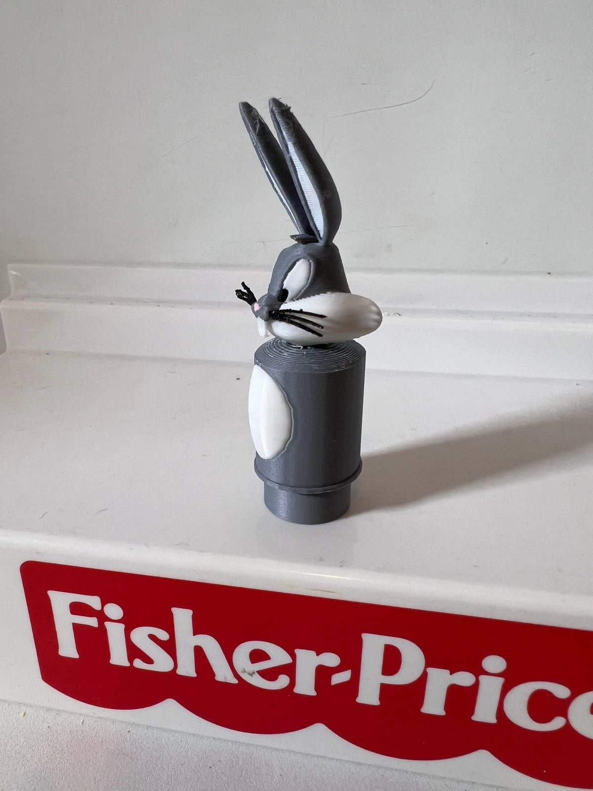 Bugs Bunny figurine with raised ears on black base atop white Fisher-Price label