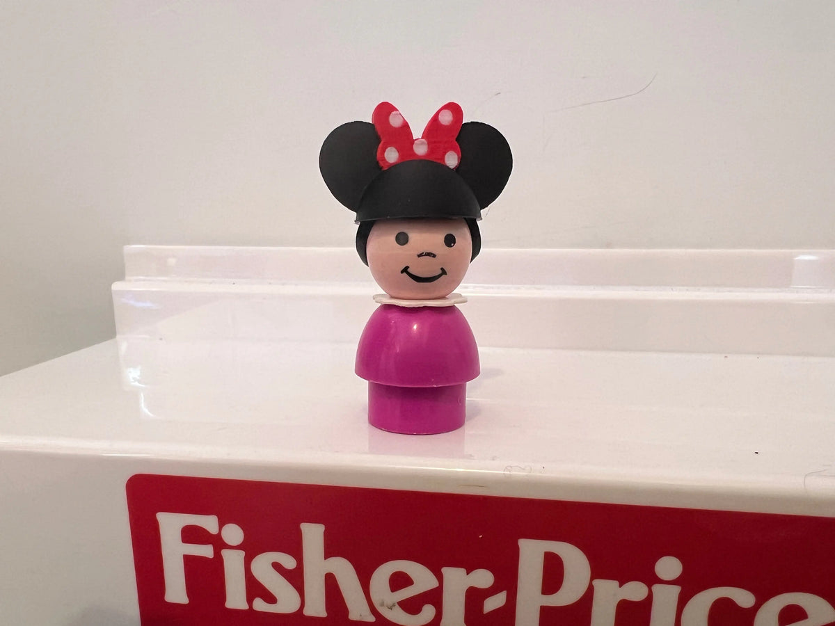 A custom 3D printed Minnie hat, with a red and white polka-dot bow, on a vintage Fisher-Price Little People figure.