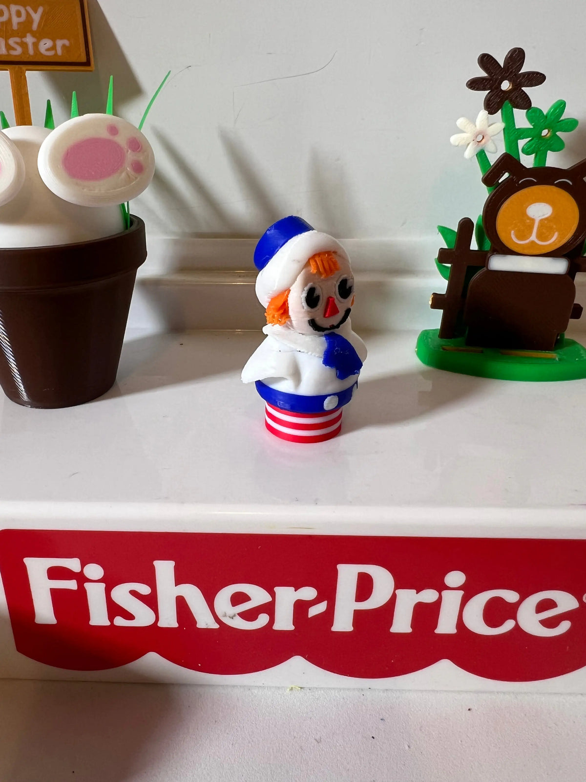 Raggedy Andy Easter doll figurine facing left, wearing blue hat and striped outfit
