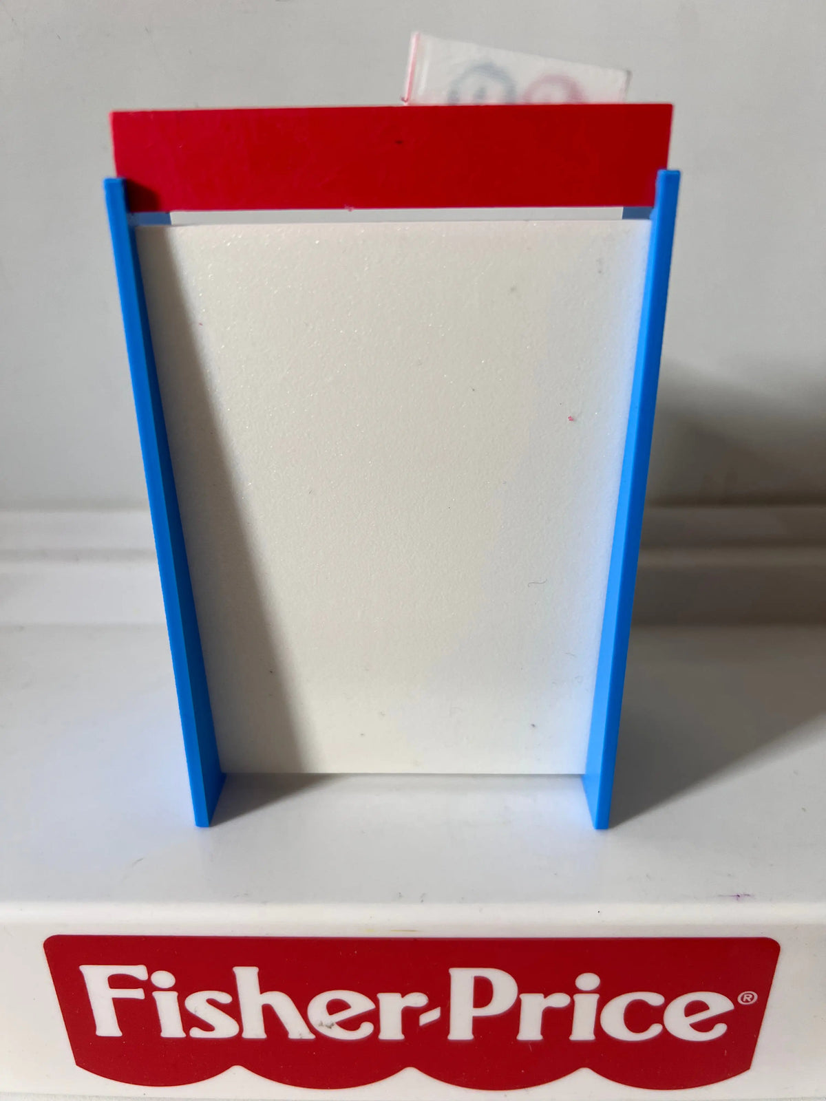 Fisher-Price toy shelf with red top bar, blue sides, and empty white shelves