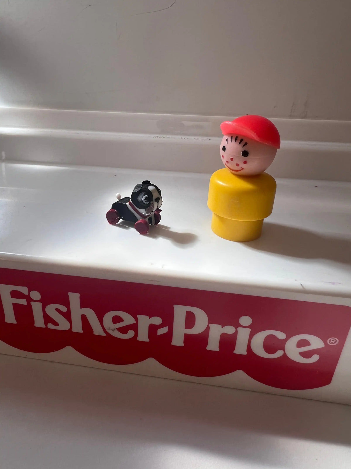 Mini child figure in red hat with yellow body and small dog on red Fisher-Price box