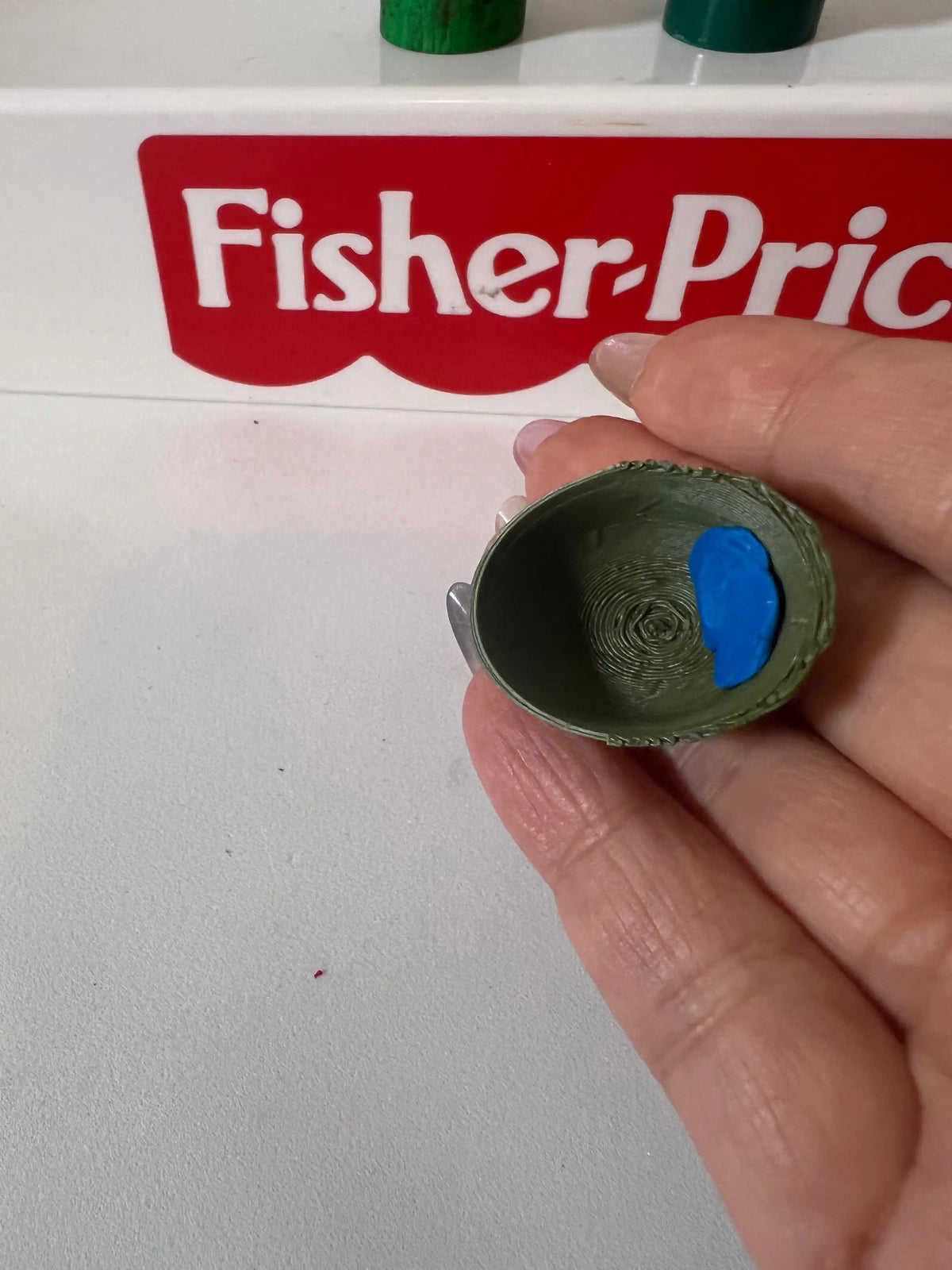 Green army-style helmet in a hand, showing textured surface and interior