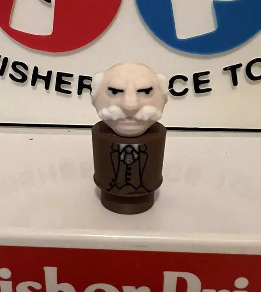 A custom 3D printed Little People figure of Muppets' Waldorf, in a brown suit, stands before a Fisher-Price sign.