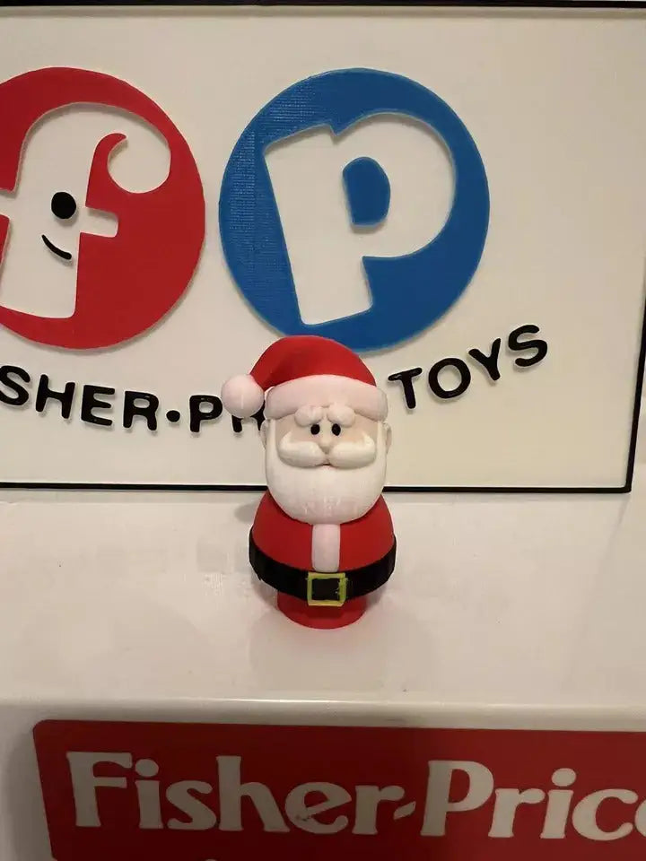 A custom 3D printed Little People Santa figure stands in front of a white sign with red and blue Fisher-Price logos.