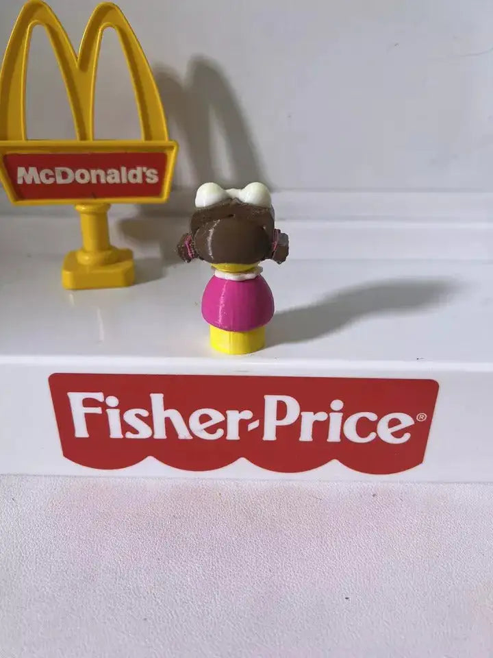 McDonald's Birdie toy figurine, back view; yellow head, black hair, pink dress, on base