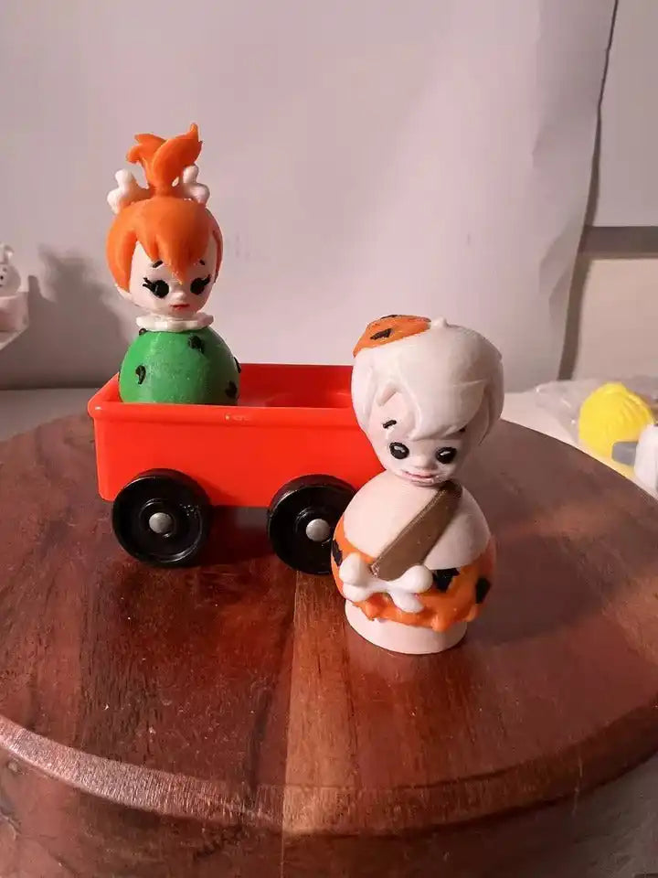 Bam Bam collectible figure in orange-and-black spots beside red toy wagon