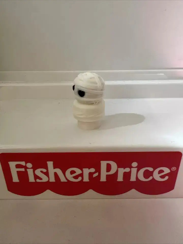 White wrapped mummy boy toy figurine, round black eye on shelf