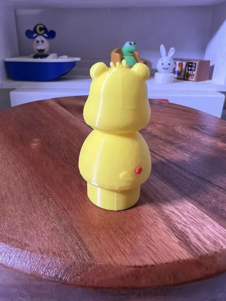 Yellow bear figurine standing sideways with small red nose