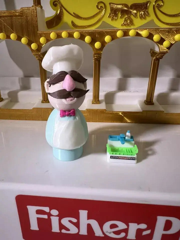 Chef puppet figurine front view, tall white hat, brown mustache, pink bow tie, light blue outfit