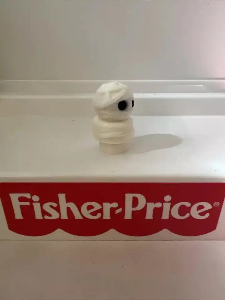 White wrapped mummy boy toy figurine with one black eye, on shelf