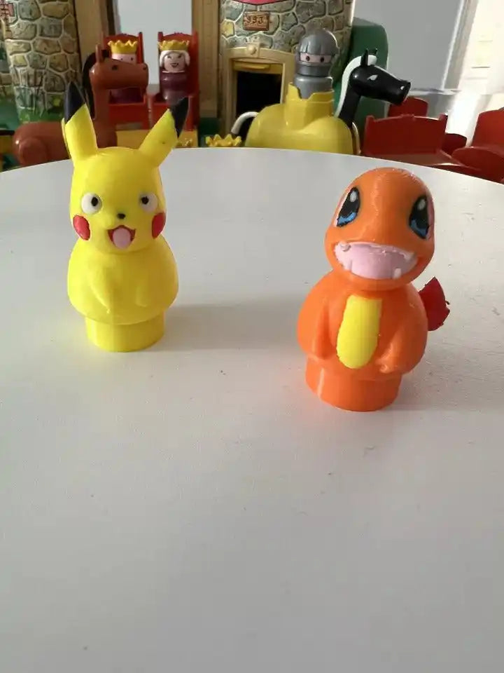 A custom 3D printed yellow Pikachu figure and orange Charmander figure, Little People style, on a white surface.