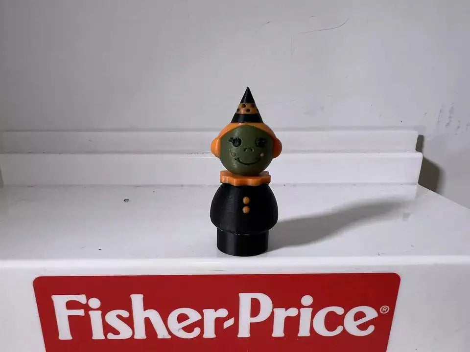 Halloween witch figurine with black dress and hat, green face and orange/brown collar.