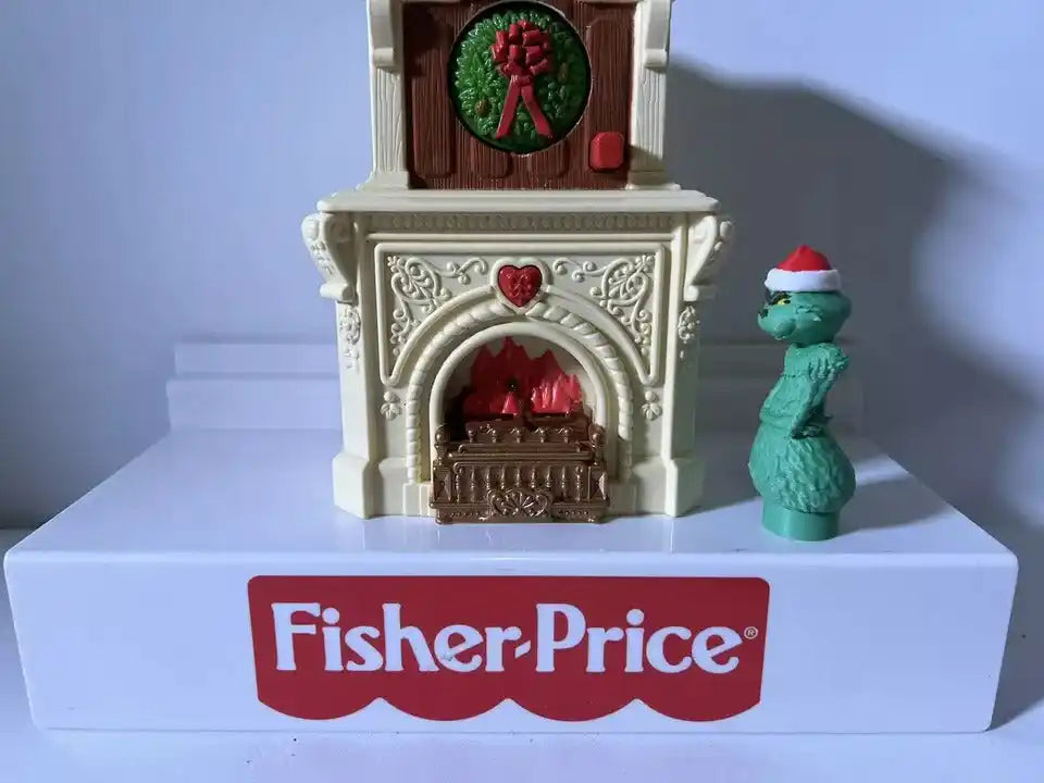 Fisher-Price holiday Grinch figure standing by white fireplace with red heart arch