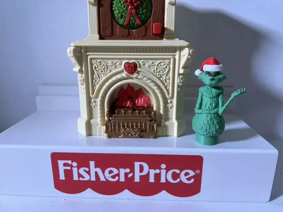 Fisher-Price holiday Grinch figure beside white fireplace playset with red hearth