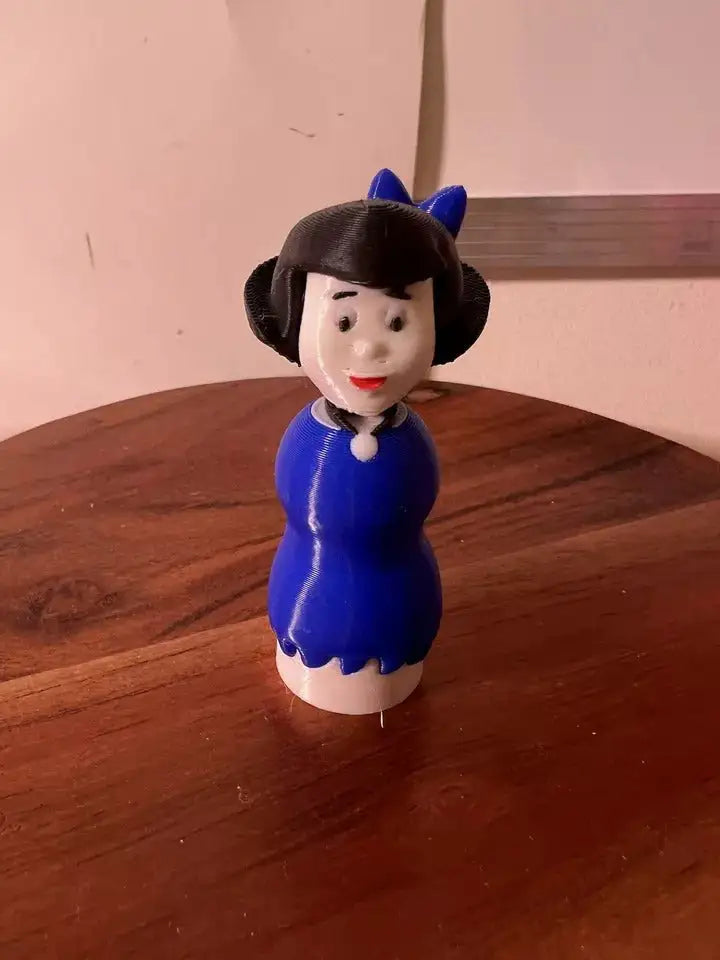 A 3D printed custom "Flintstones Betty" Little People figure in a blue dress stands on a wooden surface.