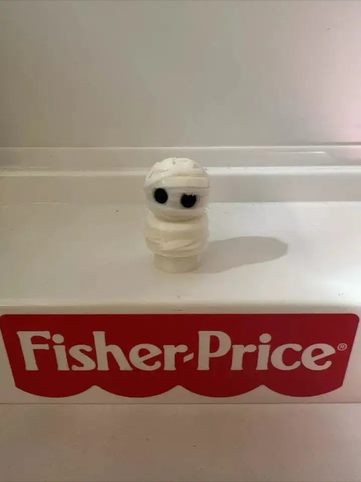 A custom Fisher-Price Little People Halloween Mummy Boy figure stands on a white surface with the red Fisher-Price logo.