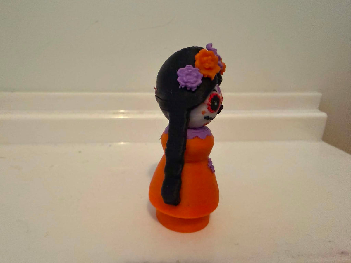 Catrina-style girl figurine side view with orange dress and flower headpiece