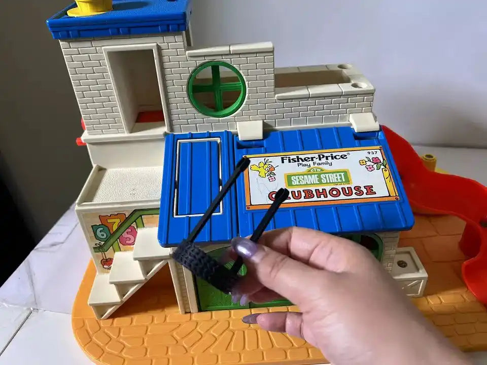 Hand holding dark gray tire swing, with Fisher-Price Sesame Street Clubhouse toy playhouse