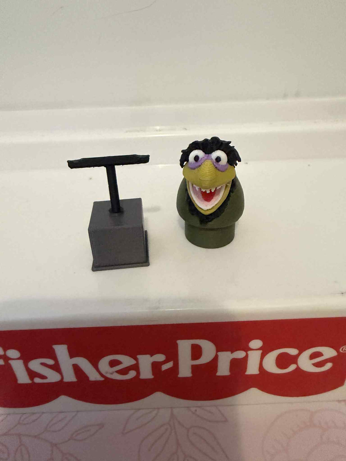 Laughing green muppet head with purple glasses, on dark stand base