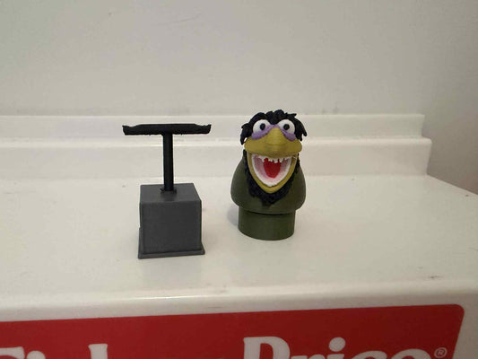 Green muppet figure with open mouth and purple glasses, on dark stand