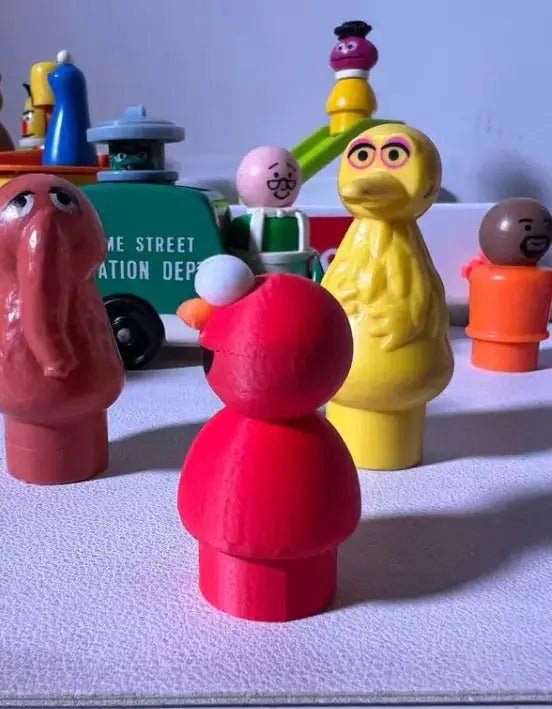 3D-printed cartoon figure: front pink figure with white hands, yellow figure beside