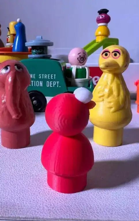 3D-printed cartoon figure: pink figure facing yellow figure, with green and gray figures behind