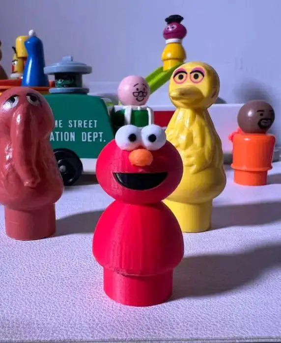 A red 3D-printed custom Elmo Little People figure stands with Big Bird and other vintage-style figures on a light surface.