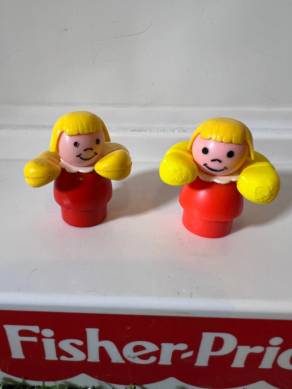 Fisher-Price toy figure pair with yellow hair and red bodies on shelf