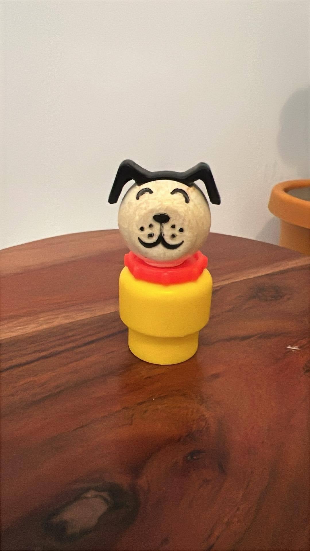 Dog-shaped toy figure with yellow base and red collar on wooden table