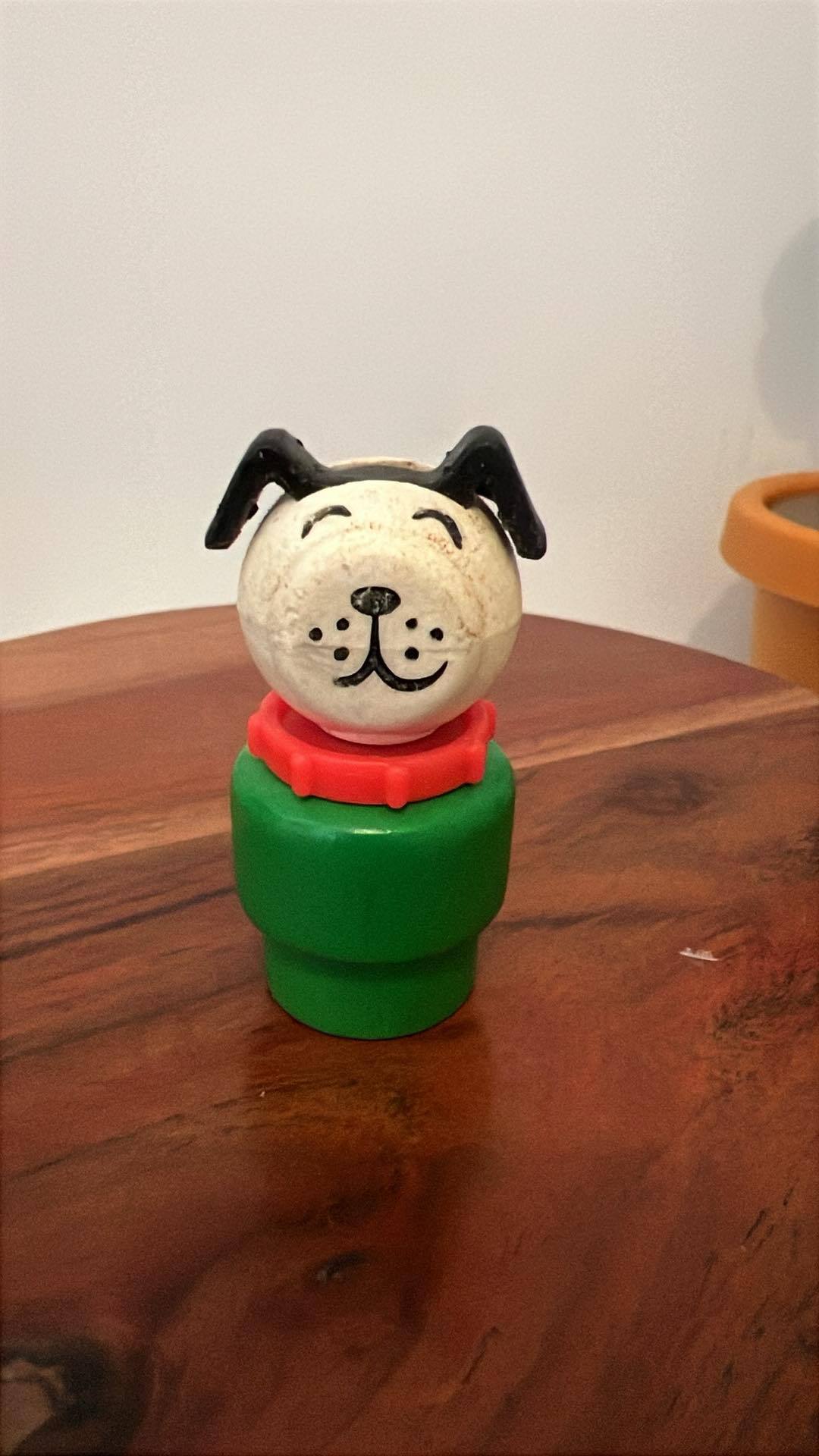 Dog-shaped toy figure with green base and red collar on wooden table