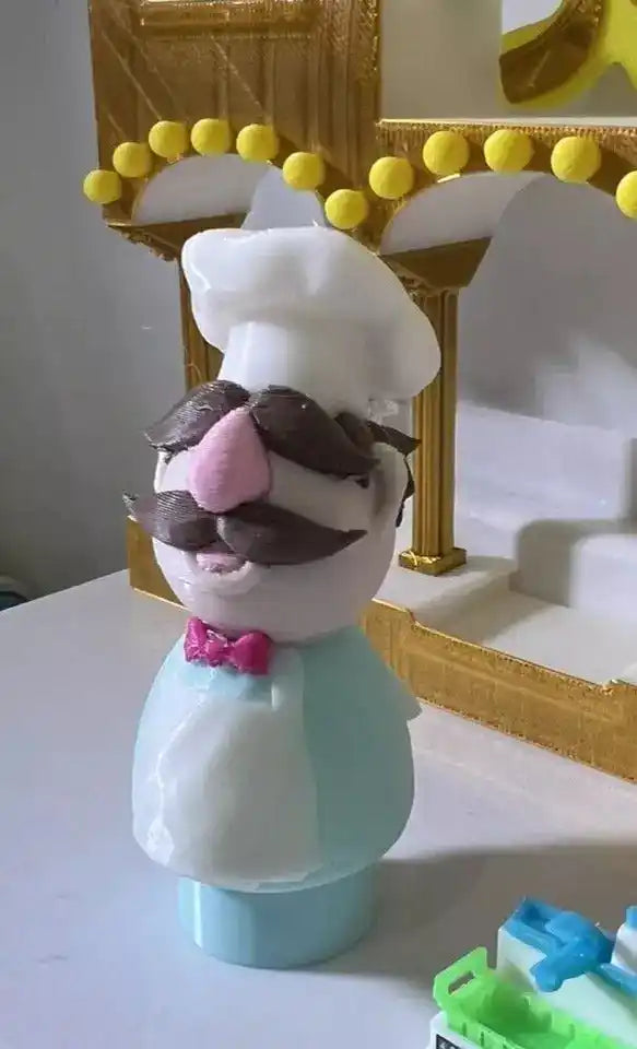Swedish chef puppet figurine with white hat, brown mustache, pink bow tie, light blue outfit