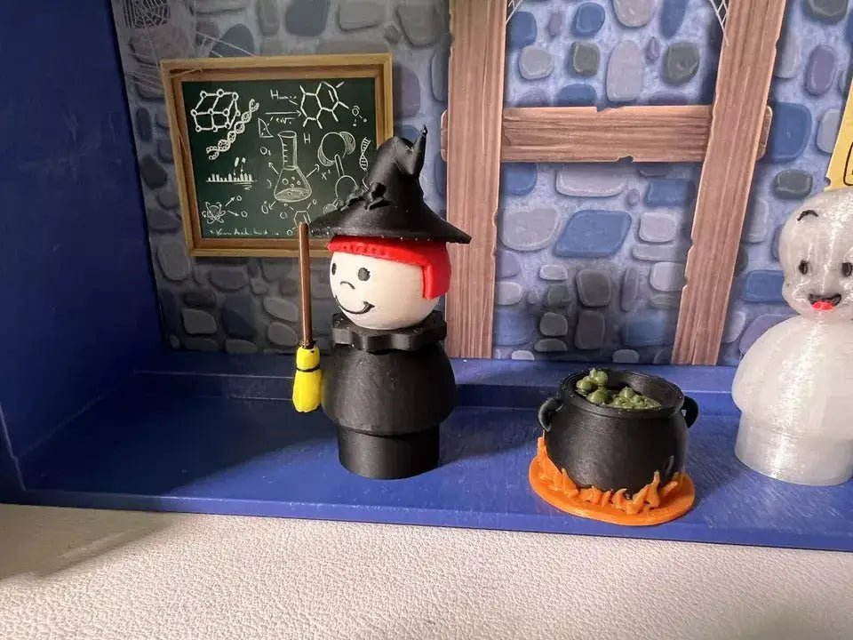 Halloween witch figurine with broom beside black cauldron with orange base