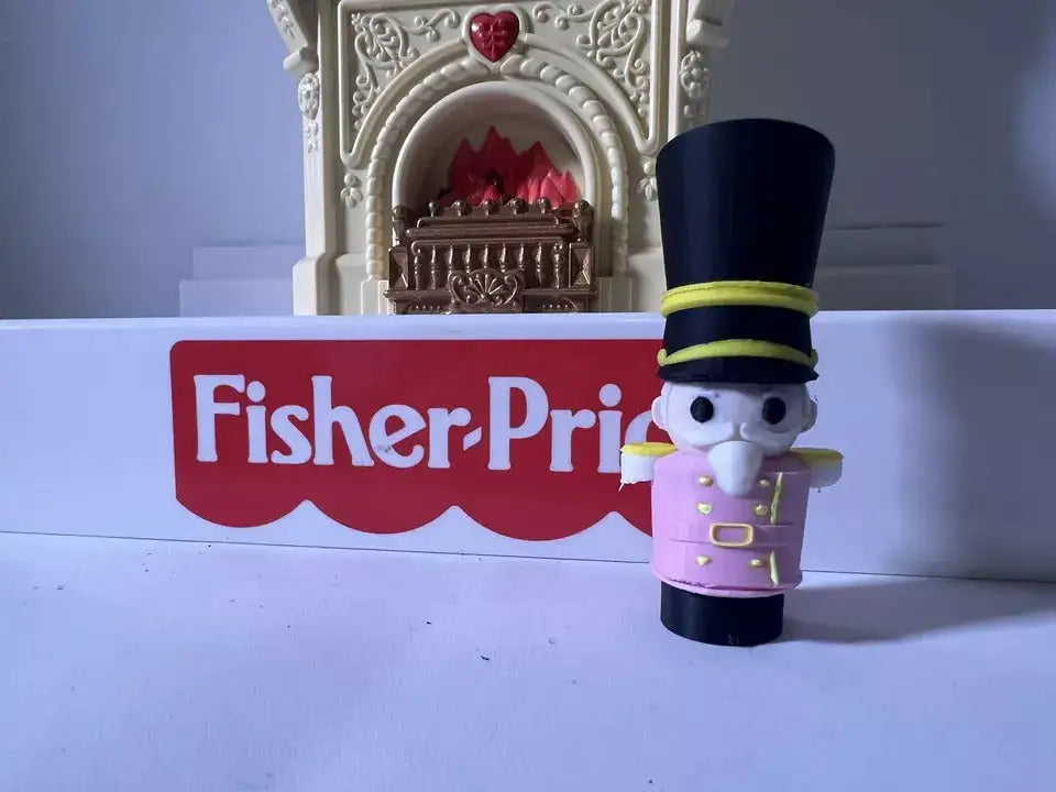A custom 3D printed Little People-sized Christmas Nutcracker figure stands in front of a Fisher-Price logo.