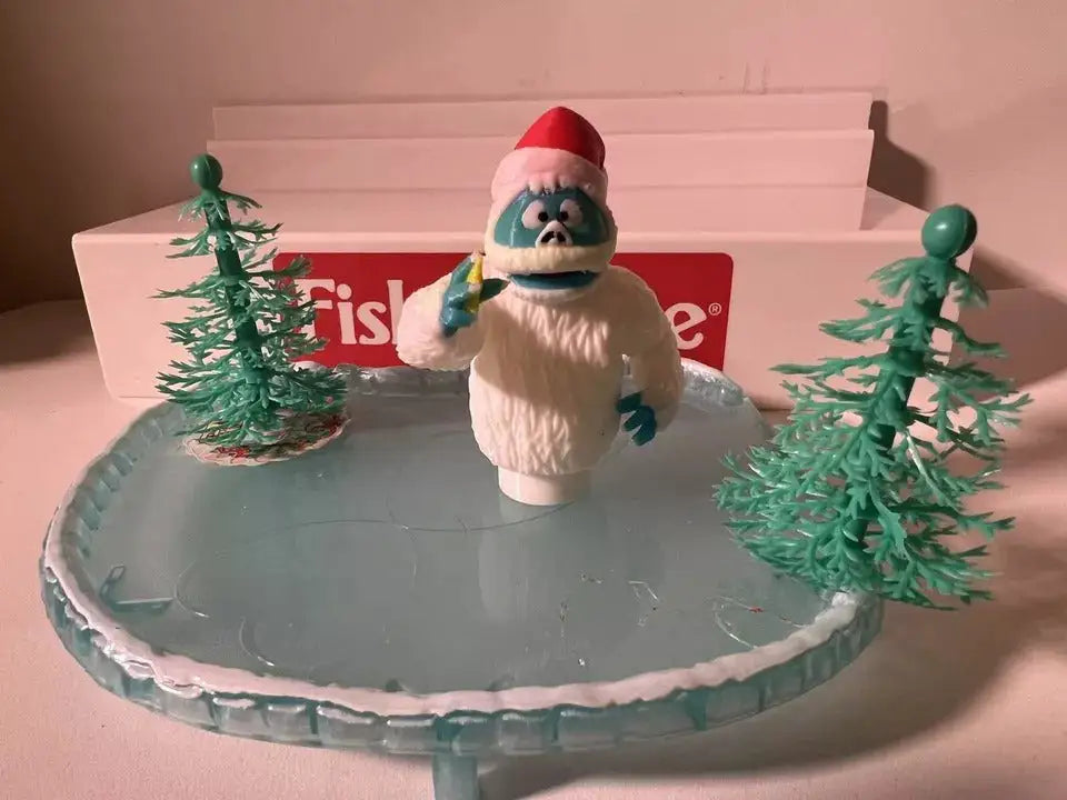 Holiday yeti figure in white fur with red hat holding a small sign, on gray base