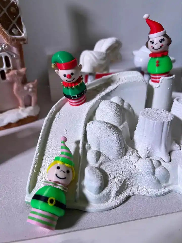 Three holiday figures: green-banded elf, red-hat snowman, and small elf on snowy base