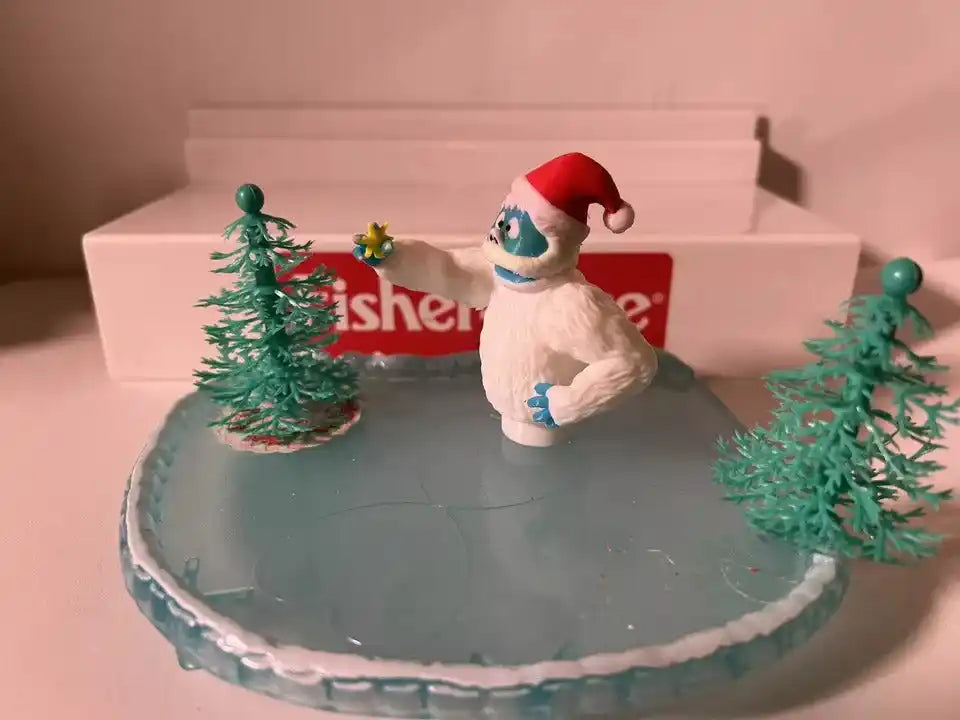Holiday yeti decoration with red Santa hat on gray base with two green pine trees