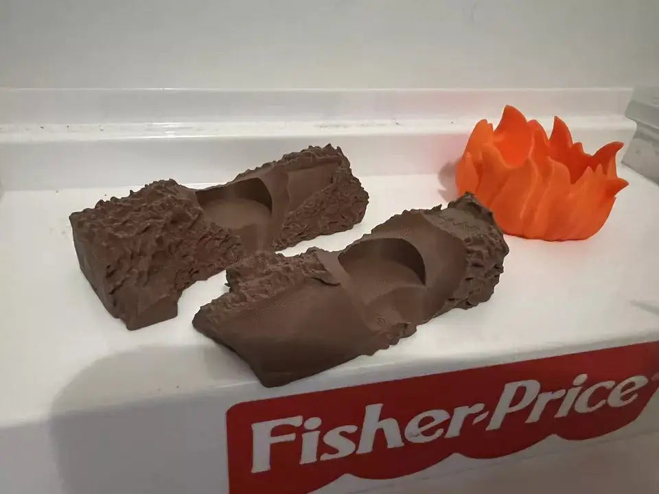 Two brown custom 3D-printed logs and an orange 3D-printed fire pit for a Fisher-Price Little People campfire set.