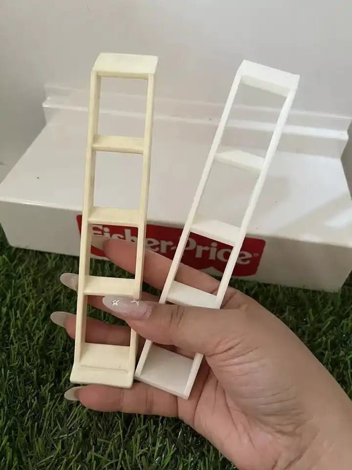 A hand holds two small, off-white Fisher-Price Little People A-Frame ladders against a green and white background.